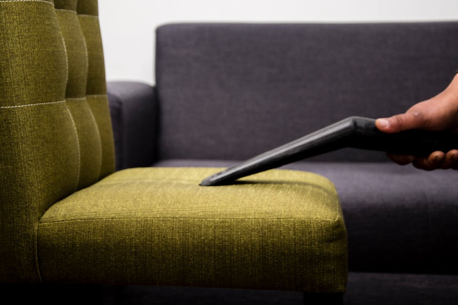 Close-up of a vintage sofa in a residential living room with floral upholstery fabric, illuminated by natural sunlight streaming through a window. The sofa features decorative cushions in shades of cr